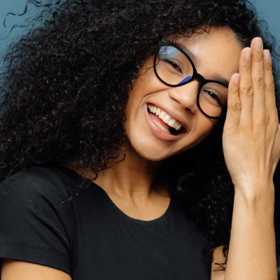 close-uportrait-happy-african-american-female-laughs-something-funny-has-positive-expression-wears-glasses-has-curly-hair-dressed-casually-closes-eyes-with-happiness-isolated-pink